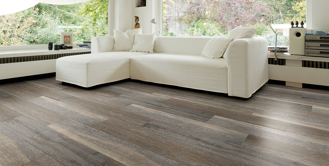 Heller Wohnraum mit Holzoptikboden, weißem Sofa und großen Fenstern